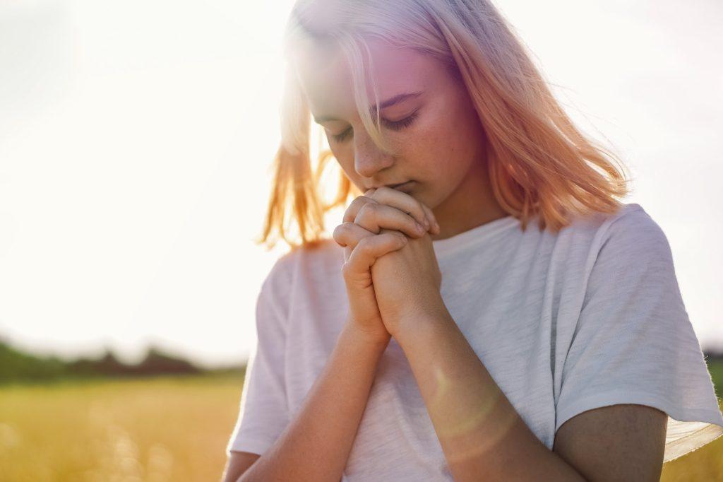 Girl closed her eyes, praying in a field. Hands folded in prayer concept for faith